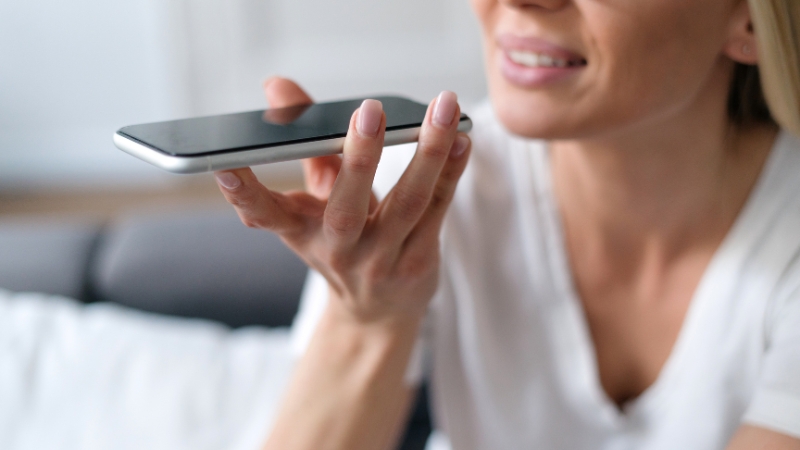 A woman speaks into her smartphone voice assistant, showing a natural moment of voice search use for local consumer intent