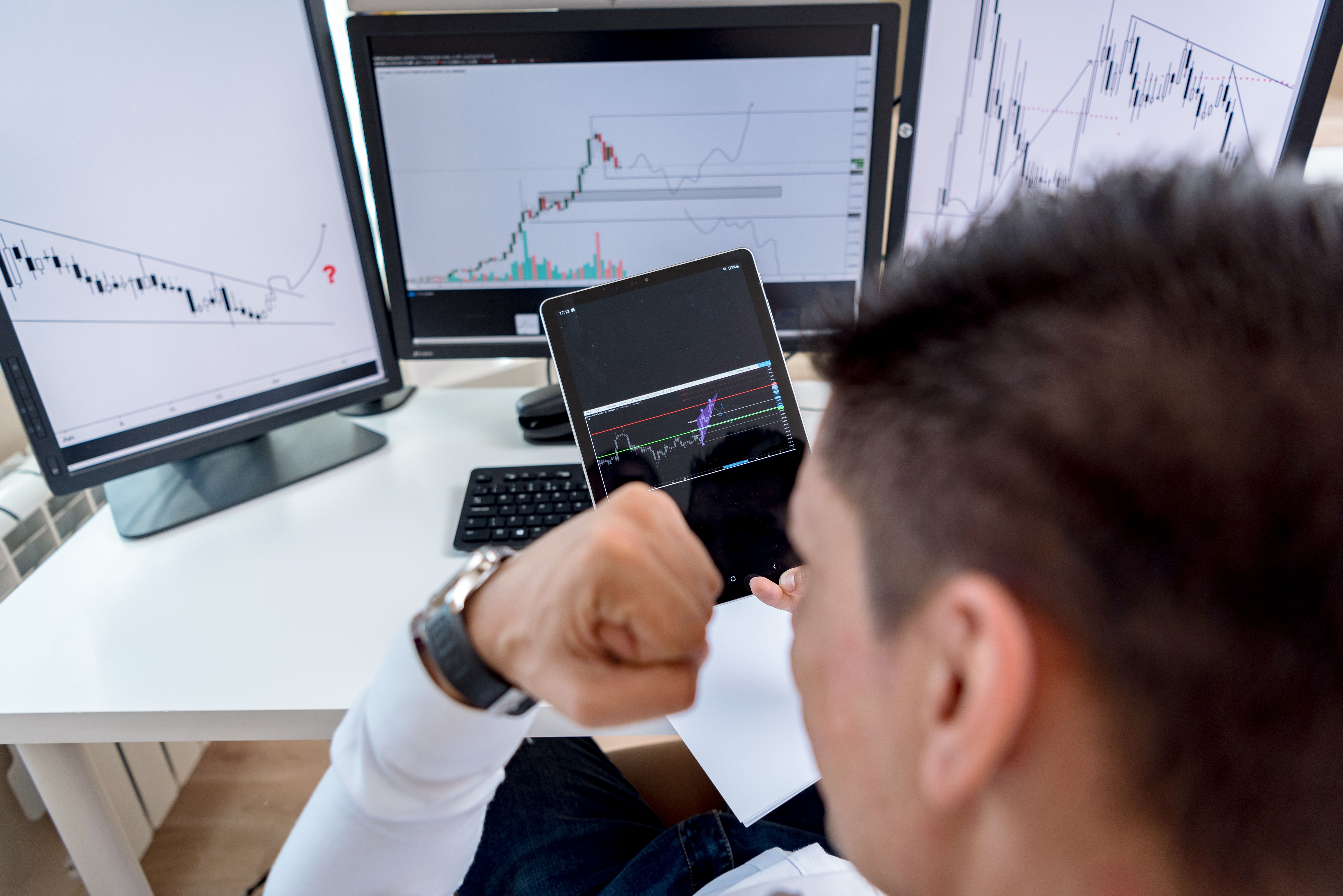 Trader studying market charts across multiple monitors at a workstation.